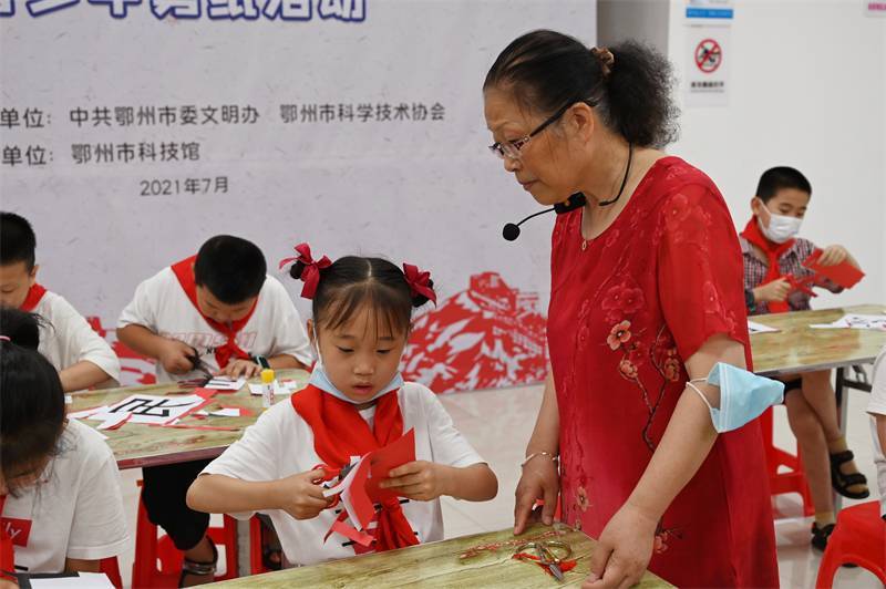 2021年7月10日，鄂州市科協(xié)組織落駕坪小學(xué)學(xué)生在鄂州市科技館開展社會(huì)主義核心價(jià)值觀系列活動(dòng)，圖為開展的紅色剪影圓夢(mèng)中華剪紙活動(dòng)，老師指導(dǎo)同學(xué)剪紙.jpg